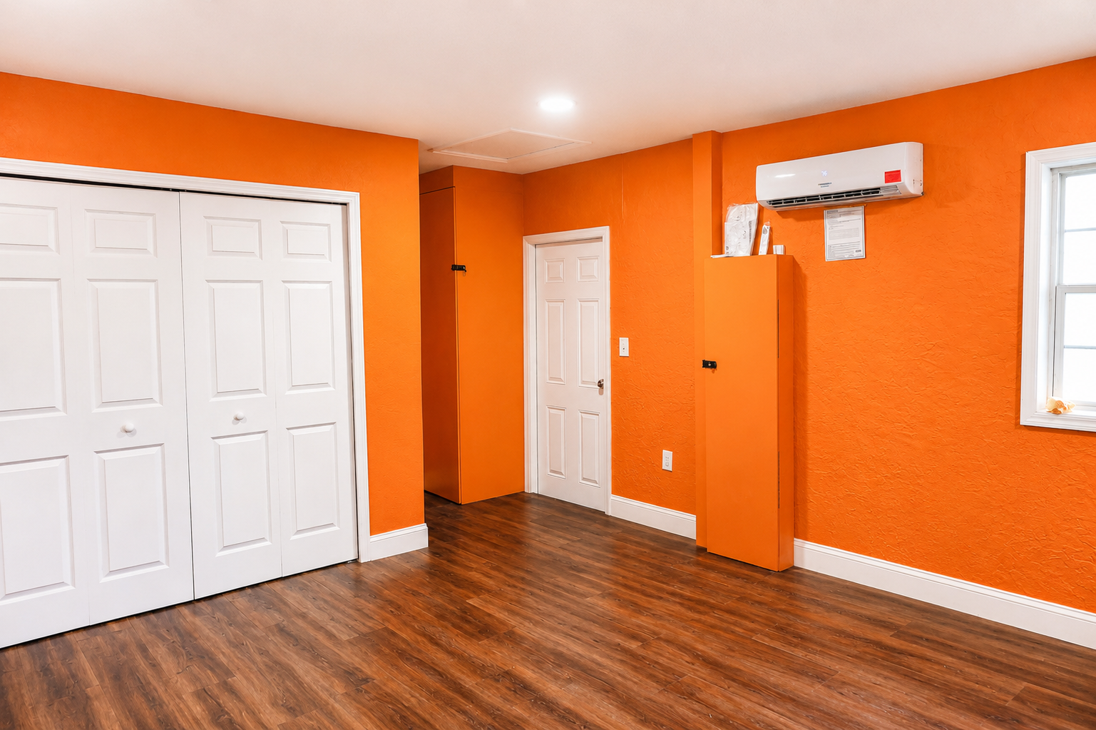 Garage conversion in Tampa, FL finished as a bedroom with wood-look vinyl flooring, a ductless mini-split AC, closet doors, and orange accent walls.