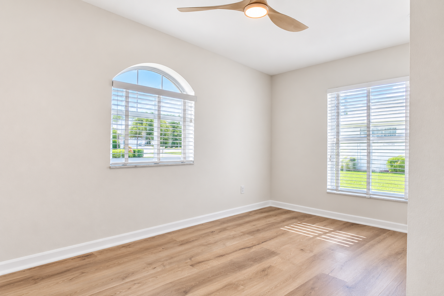 Bright bedroom after renovation in Tampa, FL with warm oak-tone vinyl plank flooring, white blinds, and a modern ceiling fan.
