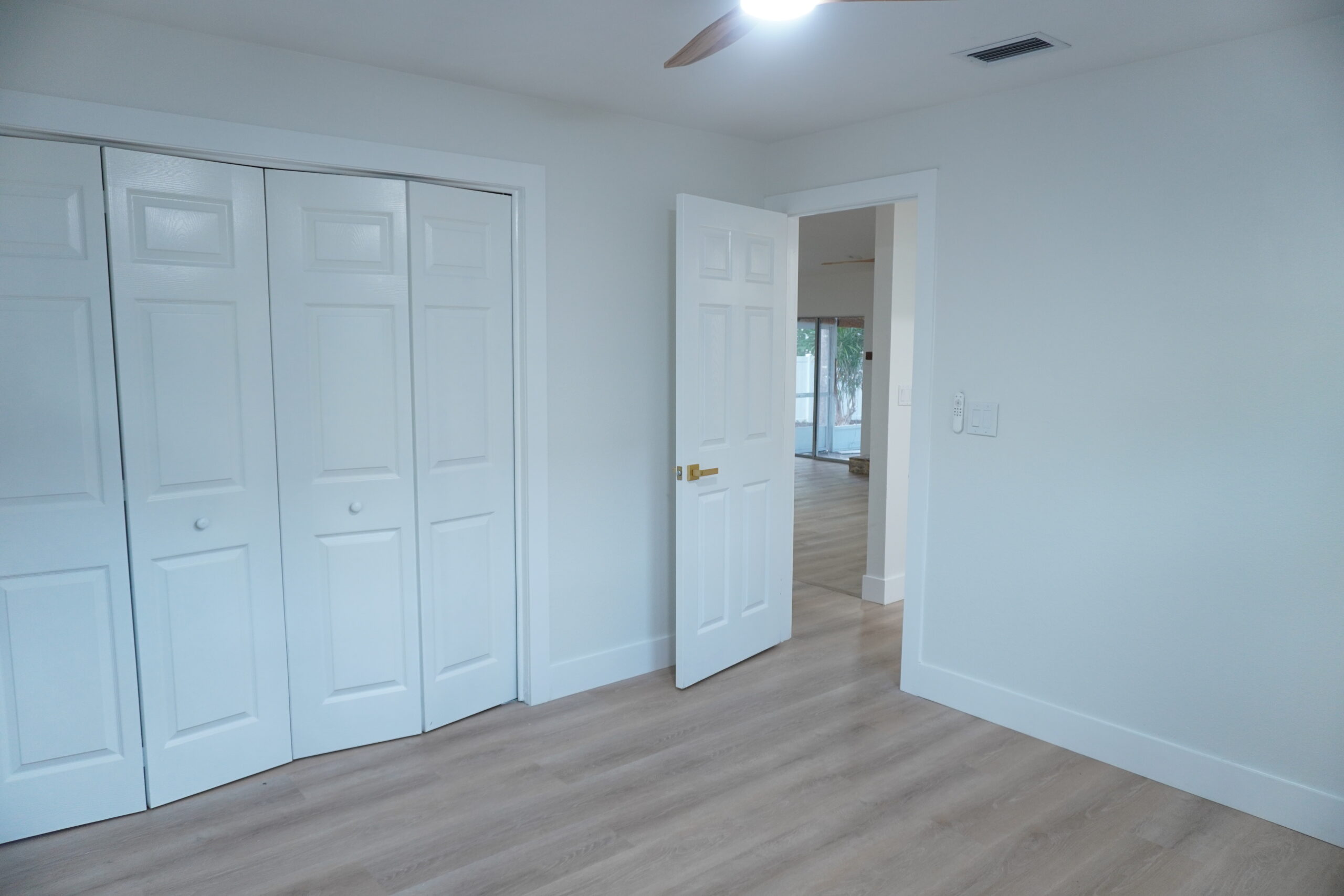 Renovated bedroom in Tampa, FL with light gray wood-look vinyl plank flooring, new white six-panel doors, bifold closet doors, and fresh white paint.