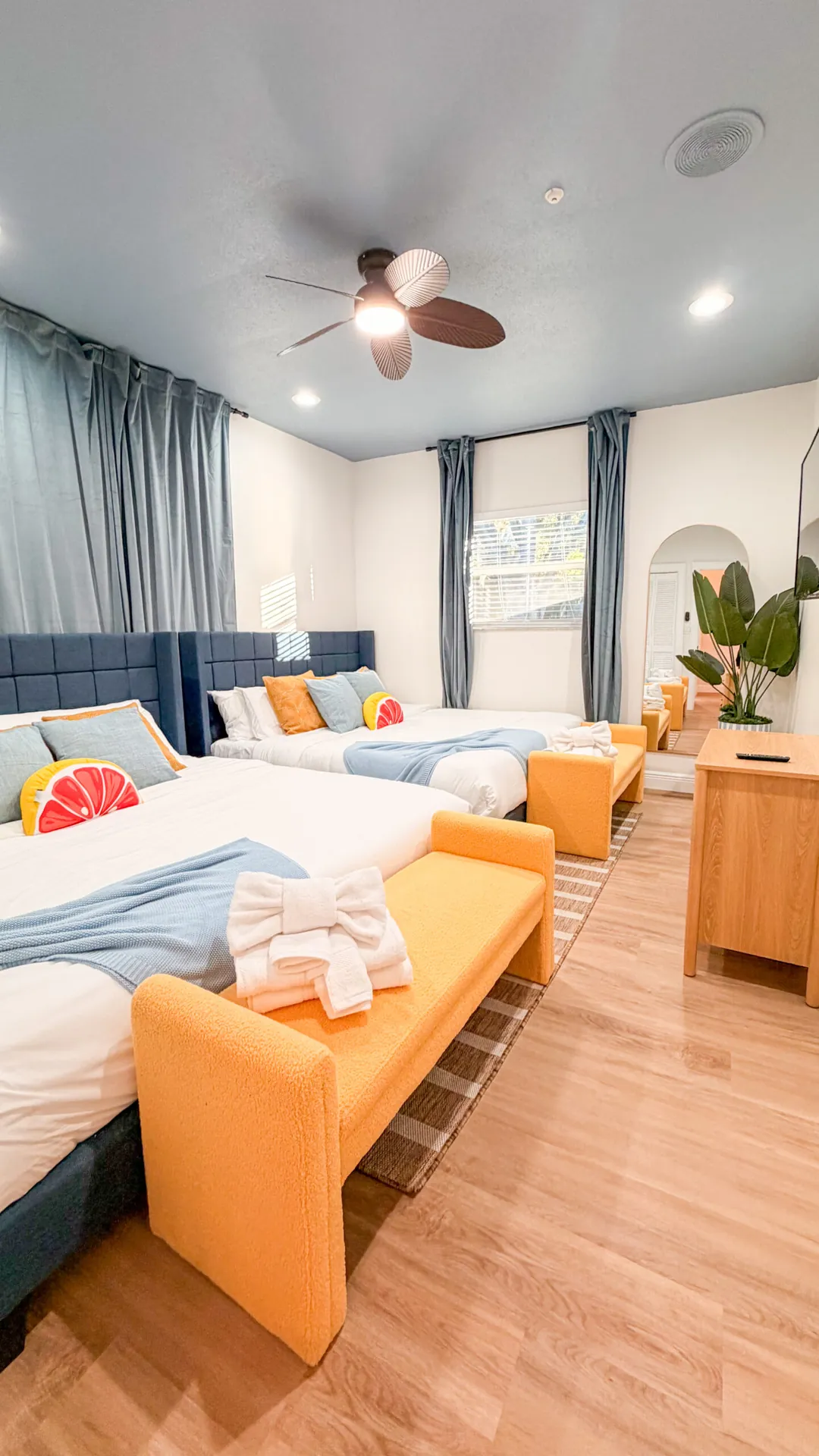 Vacation rental bedroom with navy upholstered headboards, citrus-themed decor, and orange accent benches renovated by CAG Proma