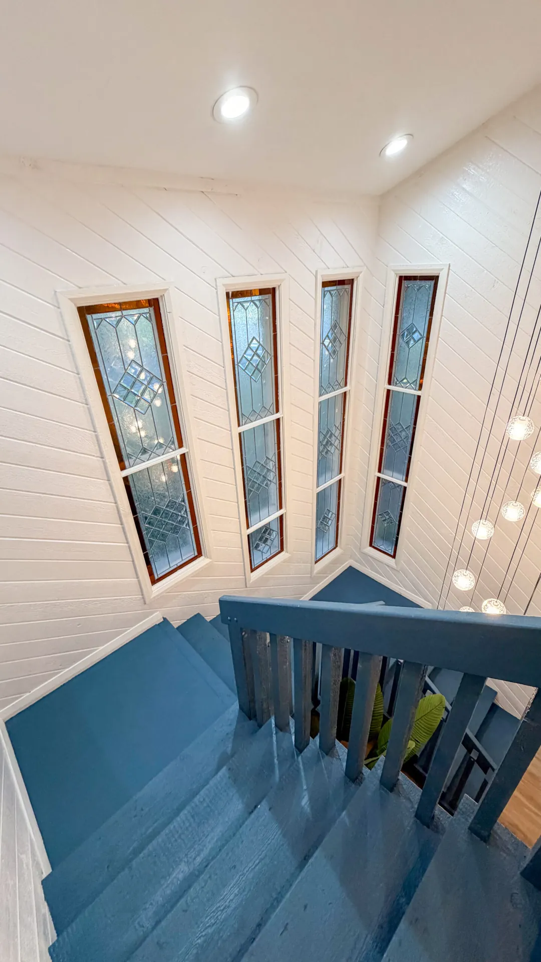 Renovated staircase with original stained glass windows and blue-painted steps in a Tampa home renovation by CAG Proma
